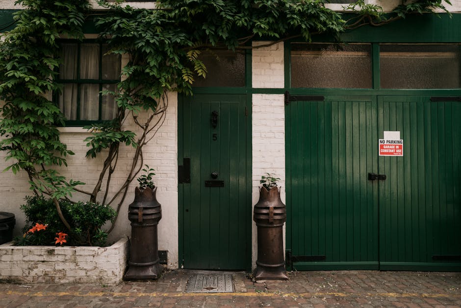 A vibrant garden scene in front of a traditional red brick terraced house features a variety of plants, including tall, yellow-flowering bushes with multiple blossoms on each stem, surrounded by lush,